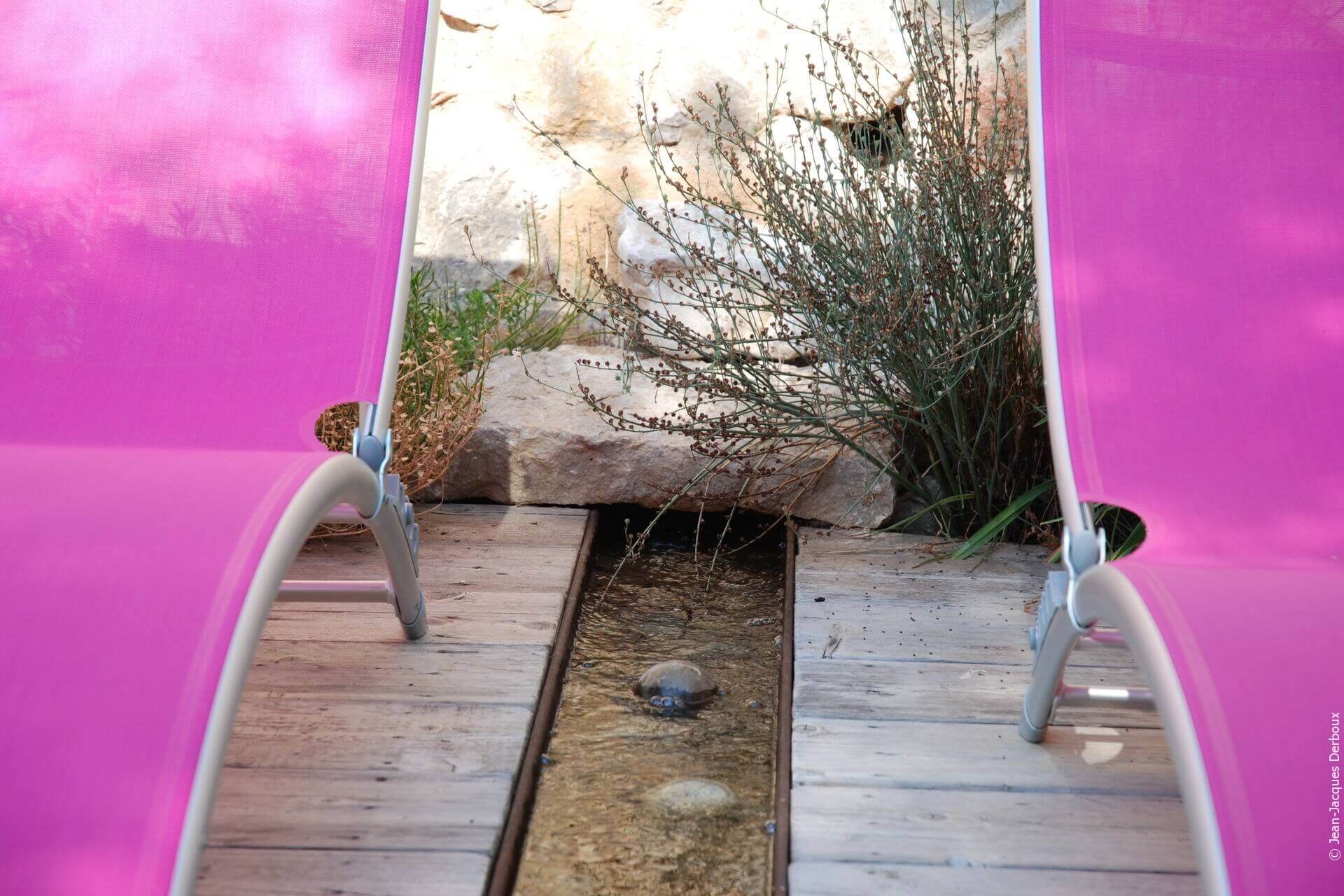 Canal en métal brut implanté dans terrasse bois, bain de soleil, sortie d’eau dans un mur.