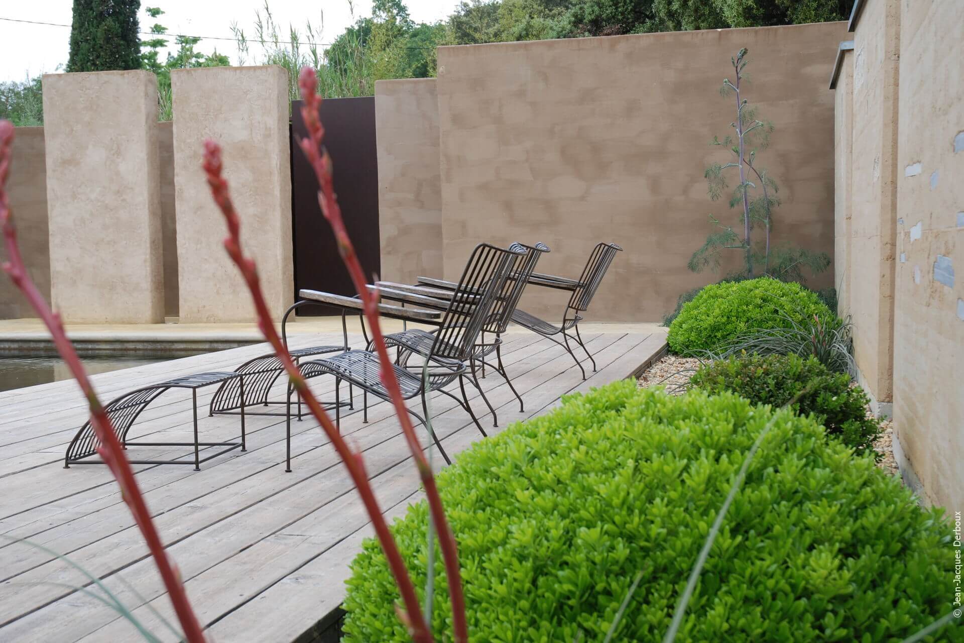 Chaise longue en métal, terrasse bois bord de piscine, mur enduit pigment naturel, végétaux topiaires.